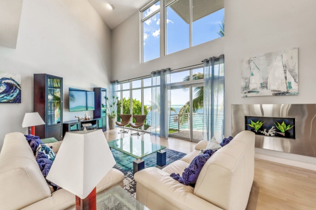 Bright, professionally staged living room in a Sarasota waterfront home with floor-to-ceiling windows, white leather seating, and coastal-inspired decor.
